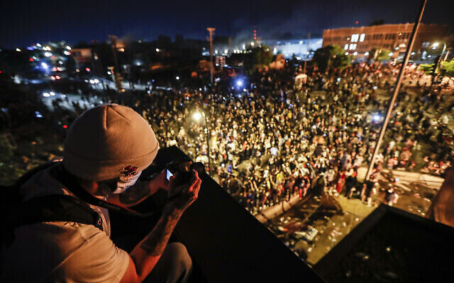 Un manifestant prend une photo lors d'une manifestation depuis le toit du 3e commissariat de police de Minneapolis, le 28 mai 2020, à Minneapolis. (Crédit : AP / John Minchillo) Un manifestant prend une photo lors d'une manifestation depuis le toit du 3e commissariat de police de Minneapolis, le 28 mai 2020, à Minneapolis. (Crédit : AP / John Minchillo)