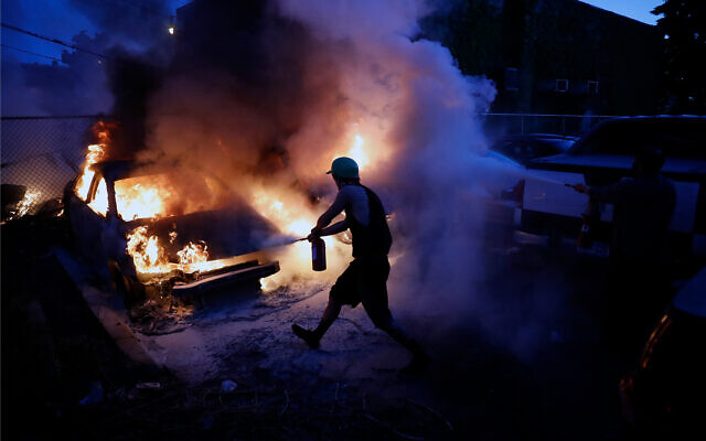Des gens tentent d'éteindre des voitures en feu lors d'une manifestation contre la mort de George Floyd à Minneapolis, Minnesota, le 29 mai 2020. (Crédit : AP / John Minchillo)