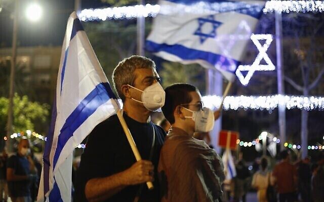 Un couple portant des masques de protection contre la propagation du coronavirus brandit des drapeaux israéliens lors d'une manifestation contre le gouvernement, sur la place Rabin à Tel Aviv, le 2 mai 2020. (AP Photo/Ariel Schalit) Un couple portant des masques de protection contre la propagation du coronavirus brandit des drapeaux israéliens lors d'une manifestation contre le gouvernement, sur la place Rabin à Tel Aviv, le 2 mai 2020. (AP Photo/Ariel Schalit)