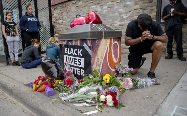 Les gens se rassemblent et prient autour d'un mémorial improvisé, le 26 mai 2020, à Minneapolis, près du site où un homme noir, qui avait été placé en garde à vue la veille, est mort. (Crédit : Elizabeth Flores/Star Tribune via AP) Les gens se rassemblent et prient autour d'un mémorial improvisé, le 26 mai 2020, à Minneapolis, près du site où un homme noir, qui avait été placé en garde à vue la veille, est mort. (Crédit : Elizabeth Flores/Star Tribune via AP)
