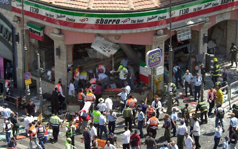 La police et les secouristes entourant la scène d'un attentat-suicide à l'intérieur de la pizzeria Sbarro, à Jérusalem, le 9 août 2001. Quinze personnes ont été tuées et 130 blessées. Une seizième victime est décédée en 2023. (Crédit : Peter Dejong/AP)