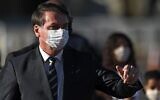 Le président brésilien Jair Bolsonaro, portant un masque facial, parle à ses partisans en arrivant à une réunion ministérielle au palais Alvorada à Brasilia, au Brésil, le 12 mai 2020. (Crédit : Evaristo Sa/AFP via Getty Images)