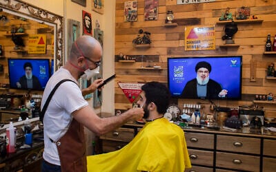 Un barbier portant un masque pour limiter la propagation du nouveau coronavirus écoute un discours du chef du Hezbollah Sayyed Hassan Nasrallah diffusé sur la chaîne de TV du Hezbollah  al-Manar, pour marquer la Journée Al-Quds (Jérusalem) alors qu'il coupe les cheveux d'un client dans son salon situé dans la banlieue sud de Beyrouth au Liban, le vendredi 22 mai 2020. (AP Photo/Hassan Ammar)