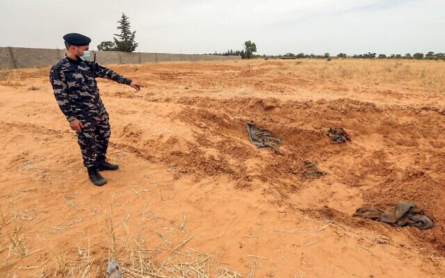 Un membre des forces de sécurité affilié au ministère de l'Intérieur du gouvernement libyen d'accord national (GNA) pointe le site signalé d'un charnier dans la ville de Tarhuna, à environ 65 kilomètres au sud-est de la capitale Tripoli, le 11 juin 2020. (Crédit : MAHMUD TURKIA / AFP)