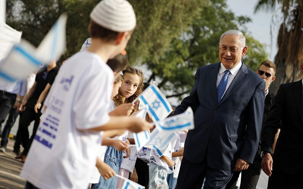 Le Premier ministre Benjamin Netanyahu, à droite, salue les élèves brandissant des drapeaux israéliens lors d'une cérémonie organisée lors de la rentrée scolaire dans l'implantation d'Elkana, en Cisjordanie, le 1er septembre 2019. (Crédit : Amir Cohen/Pool via AP)