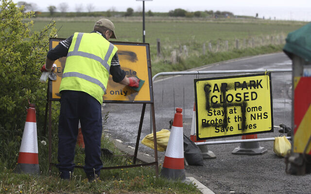 Un employé nettoie une croix gammée peinte à l'entrée d'une route et d'un parking fermé à Northumberland,  en Angleterre, le 30 avril 2020 (Crédit : Owen Humphreys/PA via AP)