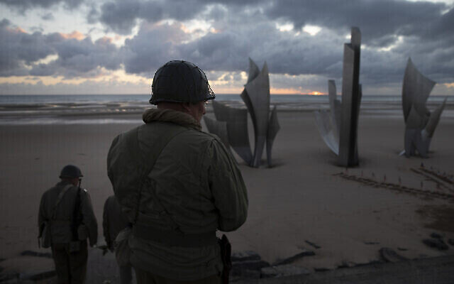 Deux hommes portant des uniformes de la Deuxième guerre mondiale marchent vers le monument des Braves au lever du soleil avant la 76ème cérémonie du Débarquement à Saint Laurent sur Mer en Normandie en France, le samedi 6 juin 2020. (AP Photo/Virginia Mayo)