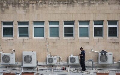 Un ouvrier installant des climatiseurs sur le toit d'un immeuble de bureaux dans le centre de Jérusalem, le 8 février 2018. (Crédit : Nati Shohat/Flash90)