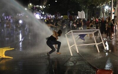 Une manifestante glisse alors que la police fait usage de canons à eau pendant des heurts lors de la manifestation anti-Netanyahu à Jérusalem, le 14 juillet 2020. (Crédit : MENAHEM KAHANA / AFP) Une manifestante glisse alors que la police fait usage de canons à eau pendant des heurts lors de la manifestation anti-Netanyahu à Jérusalem, le 14 juillet 2020. (Crédit : MENAHEM KAHANA / AFP)
