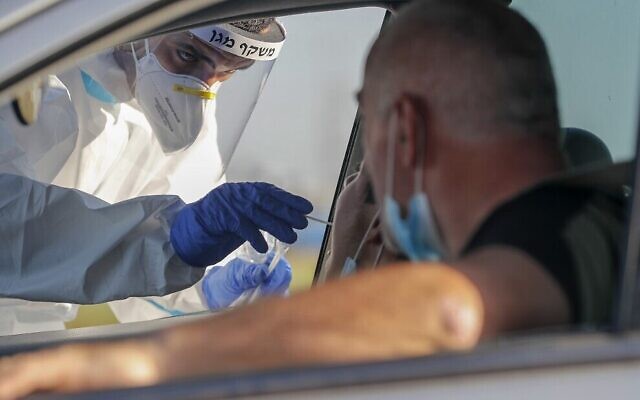 Un personnel médical du Magen David Adom prélève un échantillon pour un dépistage de la COVID-19 dans un centre de dépistage de type dirve-in dans la ville israélienne de Lod, le 15 juillet 2020. (Crédit : AHMAD GHARABLI / AFP) Un personnel médical du Magen David Adom prélève un échantillon pour un dépistage de la COVID-19 dans un centre de dépistage de type dirve-in dans la ville israélienne de Lod, le 15 juillet 2020. (Crédit : AHMAD GHARABLI / AFP)