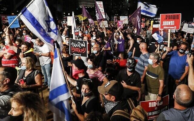 Des manifestants antigouvernementaux, masqués en raison de la pandémie de coronavirus COVID-19, se rassemblent avec des drapeaux israéliens et des pancartes lors d'une manifestation au parc Charles Clore dans la ville côtière méditerranéenne de Tel Aviv, le 18 juillet 2020. (Jack GUEZ / AFP)