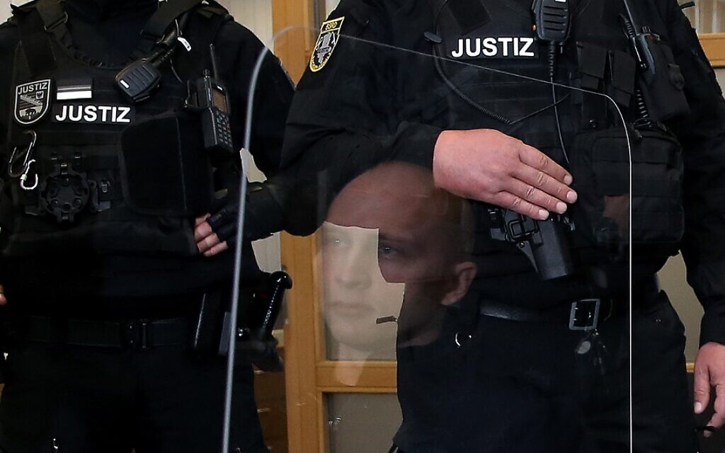 Stephan Balliet (au centre), qui est accusé d'avoir tué deux personnes après une tentative d'assaut contre une synagogue à Halle an der Saale, dans l'est de l'Allemagne, est reflété par une barrière transparente dans une salle de tribunal pour la deuxième journée de son procès, le 22 juillet 2020 à Magdeburg, en Allemagne de l'est. (Photo par Ronny HARTMANN / Sources variées / AFP) Stephan Balliet (au centre), qui est accusé d'avoir tué deux personnes après une tentative d'assaut contre une synagogue à Halle an der Saale, dans l'est de l'Allemagne, est reflété par une barrière transparente dans une salle de tribunal pour la deuxième journée de son procès, le 22 juillet 2020 à Magdeburg, en Allemagne de l'est. (Photo par Ronny HARTMANN / Sources variées / AFP)