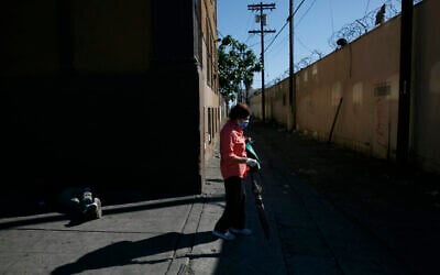 Une femme avec un masque et des gants de protection passe à côté d'un sans-abri endormi dans une rue en pleine épidémie de coronavirus dans le quartier de Westlake de Los Angeles, le jeudi 21 mai 2020. (AP Photo/Jae C. Hong)