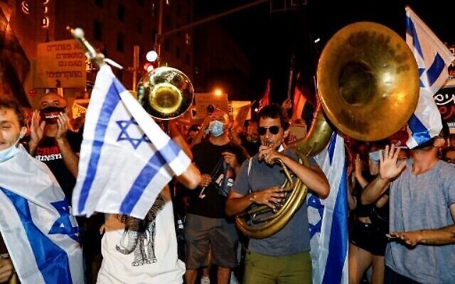 Des manifestants portant le masque pour cause de coronavirus réunis autour d'une fanfare pendant un rassemblement anti-Netanyahu organisé aux abords de la résidence officielle du Premier ministre, le 2 août 2020 (Crédit : MENAHEM KAHANA / AFP)