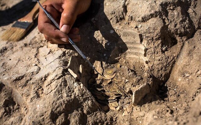 Oz Cohen, 18 ans, brosse soigneusement la terre d'un tas de pièces d'or datant du califat abbasside, lors d'une présentation à la presse des découvertes réalisées sur un site archéologique près de Tel-Aviv dans le centre d'Israël (Crédit : Heidi Levine / POOL / AFP)