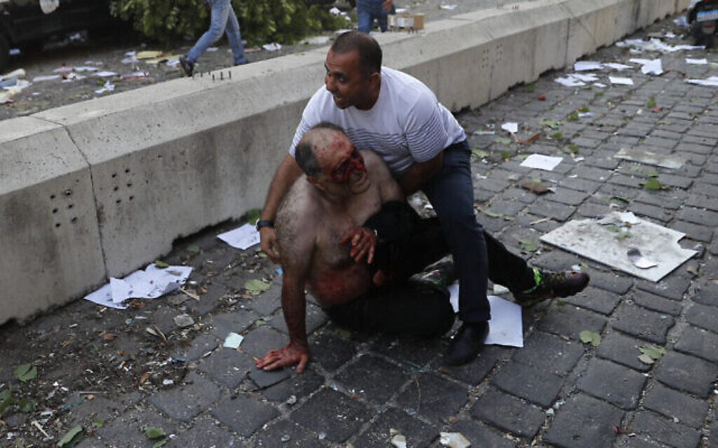 Un Libanais aide un blessé à Beyrouth, après une explosion sur le port, le 4 août 2020. (Crédit : AP Photo/Hussein Malla)