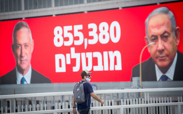 Un homme portant un masque passe devant une affiche montrant le Premier ministre Benjamin Netanyahu, à droite, et le ministre de la Défense et Premier ministre d'alternance Benny Gantz, à gauche, avec les chiffres du chômage actuels à Tel Aviv, le 22 juillet 2020 (Crédit : Miriam Alster/Flash90)