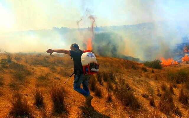 Un pompier cherche à éteindre un incendie causé par un ballon incendiaire envoyé de Gaza vers les communautés frontalières israéliennes, le 26 août 2020. (Crédit : Eshkol Regional Council)