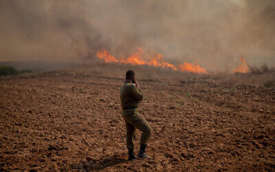 Un soldat se tient devant un incendie à proximité du kibboutz Beeri dans le sud d'Israël. L'incendie a été déclenché par un engin incendiaire accroché à un ballon depuis la bande de Gaza, le 13 août 2020. (Yonatan Sindel/Flash90)