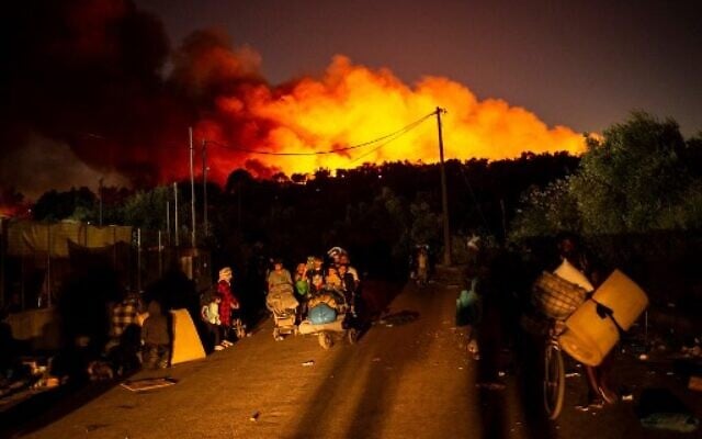 Des gens transportent leurs affaires après le déclenchement d'un vaste incendie dans le camp de migrants de Moria sur l'île grecque de Lesbos, le 9 septembre 2020. (Crédit : ANGELOS TZORTZINIS / AFP) Des gens transportent leurs affaires après le déclenchement d'un vaste incendie dans le camp de migrants de Moria sur l'île grecque de Lesbos, le 9 septembre 2020. (Crédit : ANGELOS TZORTZINIS / AFP)
