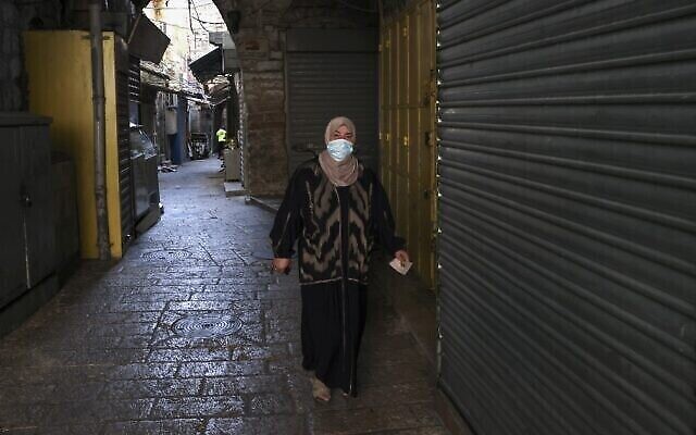 Une Palestinienne portant le masque marche dans une rue vide, avec les magasins fermés, de la Vieille Ville de Jérusalem dans le cadre du nouveau confinement national, le 19 septembre 2020 (Crédit : Menahem Kahana/AFP)