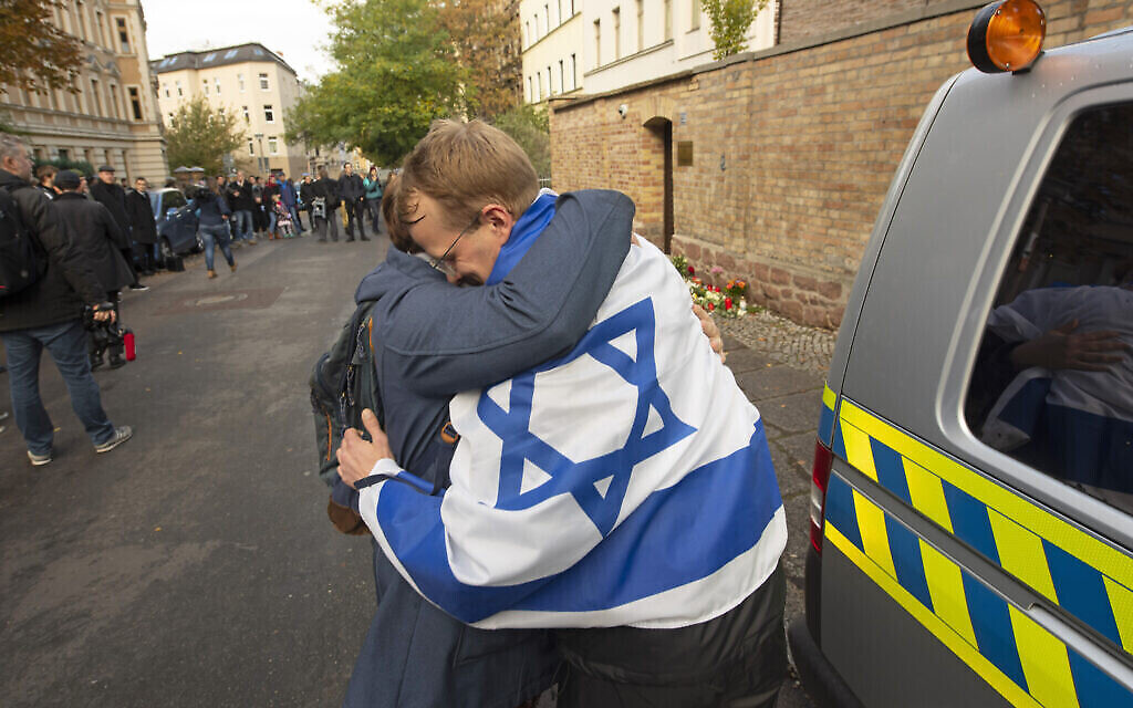 Un homme avec le drapeau israélien prend dans ses bras une autre personne devant la synagogue de Halle, en Allemagne, le 10 octobre 2019. (Crédit : AP Photo/Jens Meyer)