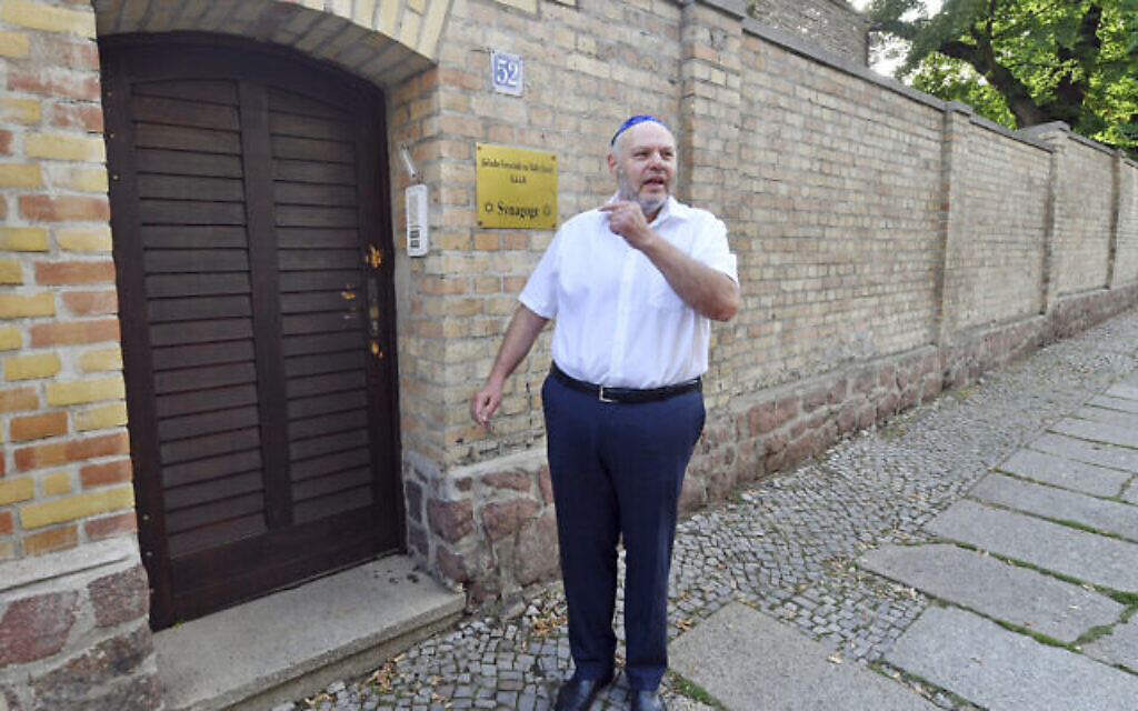 Max Privorozki, président de la communauté juive de Halle, devant la porte criblée de balle d'une synagogue avant son remplacement à Halle, en Allemagne, le 28 juillet 2020 (Crédit : Hendrik Schmidtpa/dpa via AP)