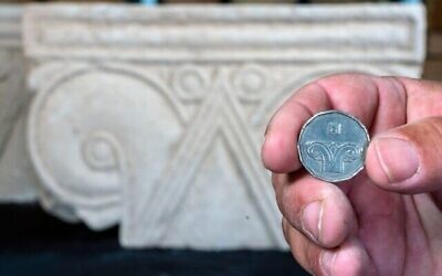 Une pièce de cinq shekels juxtaposée à une tête de colonne trouvée à Armon HaNatziv (Yaniv Berman, Autorité des antiquités d’Israël)