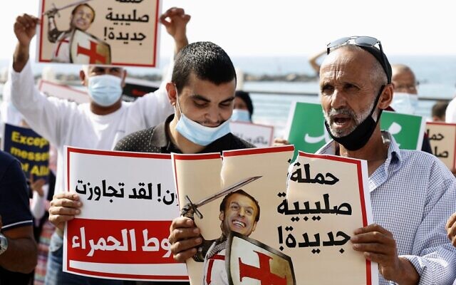 Des manifestants arabes israéliens portant le masque pour cause de coronavirus tiennent des panneaux représentant le président français Emmanuel Macron sous les traits d'un chevalier médiéval des Croisades lors d'une manifestation contre la défense, par ce dernier, des caricatures de Mahomet, près de l'ambassade de France à Tel Aviv, le 27 octobre 2020. (Crédit : JACK GUEZ / AFP) Des manifestants arabes israéliens portant le masque pour cause de coronavirus tiennent des panneaux représentant le président français Emmanuel Macron sous les traits d'un chevalier médiéval des Croisades lors d'une manifestation contre la défense, par ce dernier, des caricatures de Mahomet, près de l'ambassade de France à Tel Aviv, le 27 octobre 2020. (Crédit : JACK GUEZ / AFP)
