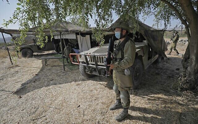 Un soldat israélien, masqué en raison de la pandémie de coronavirus COVID-19, monte la garde à côté d'un avant-poste et de véhicules militaires de transport à roues polyvalents (Humvee) lors de l'exercice militaire "Deadly Arrow" dans le nord d'Israël, le 27 octobre 2020. (Crédit : Jalaa Marey/AFP) Un soldat israélien, masqué en raison de la pandémie de coronavirus COVID-19, monte la garde à côté d'un avant-poste et de véhicules militaires de transport à roues polyvalents (Humvee) lors de l'exercice militaire "Deadly Arrow" dans le nord d'Israël, le 27 octobre 2020. (Crédit : Jalaa Marey/AFP)