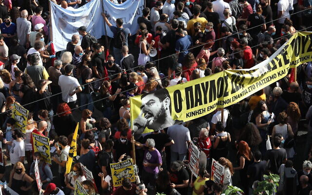 Des manifestants brandissent une bannière dépeignant le chanteur grec de rap Pavlos Fyssas, poignardé et tué par un partisan de la formation d'extrême-droite Aube dorée en 2013, aux abords du tribunal, avant le verdict qui sera rendu dans l'affaire, le 7 octobre 2020. (Crédit : AP Photo/Yorgos Karahalis) Des manifestants brandissent une bannière dépeignant le chanteur grec de rap Pavlos Fyssas, poignardé et tué par un partisan de la formation d'extrême-droite Aube dorée en 2013, aux abords du tribunal, avant le verdict qui sera rendu dans l'affaire, le 7 octobre 2020. (Crédit : AP Photo/Yorgos Karahalis)