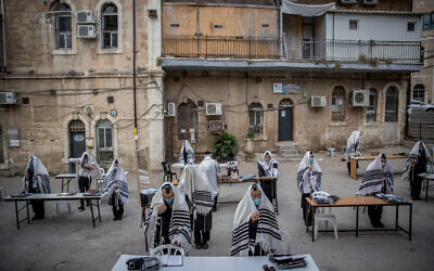 Des Juifs ultra-orthodoxes de la dynastie hassidique Karlin prient en respectant les règles de distanciation sociale devant leur synagogue à Jérusalem, le 10 août 2020. (Yonatan Sindel/Flash90)