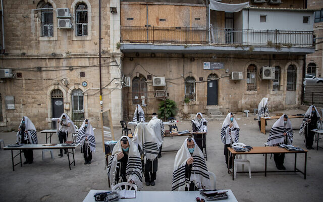 Des Juifs ultra-orthodoxes de la dynastie hassidique Karlin prient en respectant les règles de distanciation sociale devant leur synagogue à Jérusalem, le 10 août 2020. (Yonatan Sindel/Flash90)