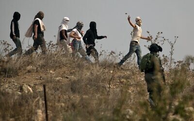 Des soldats israéliens se tiennent prêts alors que des habitants d’implantations israéliens masqués lancent des pierres sur des manifestants palestiniens (non vsisibles) qui se rassemblent lors d'une manifestation contre la construction d'un avant-poste israélien près du village palestinien de Turmusaya et de l’implantation de Shilo, au nord de Ramallah en Cisjordanie, le 17 octobre 2019. (JAAFAR ASHTIYEH/AFP)