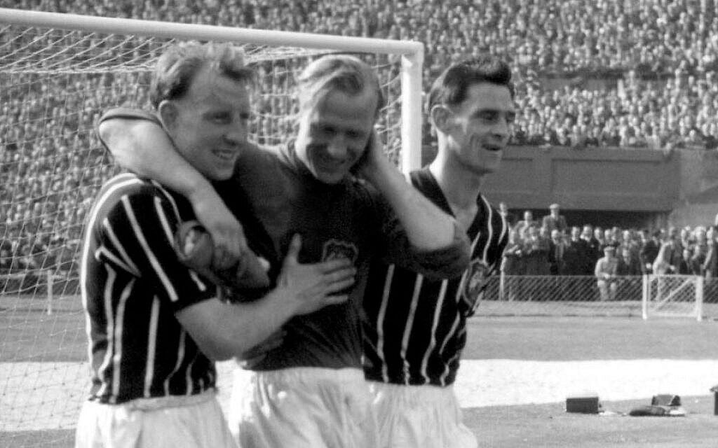 Photo du 5 mai 1956 tirée des dossiers de Bernd Trautmann, plus connu sous le nom de Bert, gardien de but de Manchester City né en Allemagne, au centre, assisté depuis le terrain par deux joueurs non identifiés, souffrant d'une fracture du cou, lors de la finale de la FA Cup contre Birmingham, au stade de Wembley à Londres. (Crédit photo : AP/PA, Dossier)