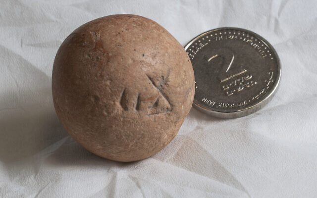 Le poids en pierre de calcaire de deux shekels, vieux de 2700 ans, à côté d'une pièce contemporaine de deux shekels (Crédit :  Shai Halevi, Autorité israélienne des antiquités)
