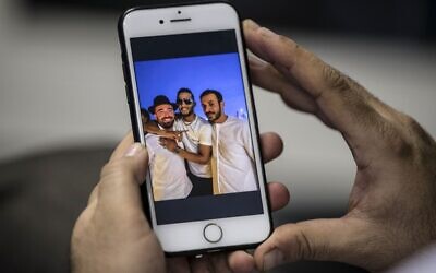Un homme au Caire tient un téléphone montrant une photo du chanteur égyptien Mohamed Ramadan publiée par la page Facebook officielle de l'État d'Israël en arabe (liée au ministère des Affaires étrangères) montrant Ramadan (au centre) enlaçant le chanteur israélien Omer Adam (à gauche) sur un toit de Dubaï, le 22 novembre 2020. (Crédit : Khaled DESOUKI / AFP)