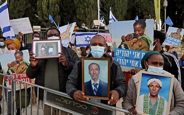 Des membres de la communauté éthiopienne israélienne brandissent des photos de leurs proches devant le bureau du Premier ministre à Jérusalem, le 25 novembre 2020. (Menahem Kahana / AFP)