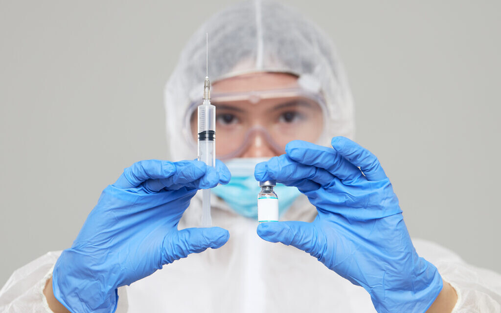 Un médecin, en habit de protection et portant le masque, avec une seringue et une dose de vaccin. (Crédit : oshcherban via iStock by Getty Images) Un médecin, en habit de protection et portant le masque, avec une seringue et une dose de vaccin. (Crédit : oshcherban via iStock by Getty Images)