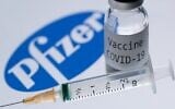 Photo d'illustration d'une seringue et d'un flacon contenant une dose de vaccin COVID-19 à côté du logo de la firme Pfizer, le 23 novembre 2020. (Crédit : JOEL SAGET / AFP)