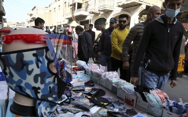 Des Irakiens passent devant des masques exposés dans un marché de rue de la capitale Bagdad le 4 décembre 2020. (Crédit : Sabah ARAR / AFP) Des Irakiens passent devant des masques exposés dans un marché de rue de la capitale Bagdad le 4 décembre 2020. (Crédit : Sabah ARAR / AFP)