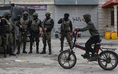 Un enfant palestinien à vélo devant des membres des forces de sécurité dans le camp de Balata, près de Naplouse en Cisjordanie, le 15 décembre 2020. (Crédit : JAAFAR ASHTIYEH / AFP)