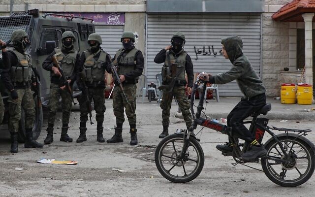 Un enfant palestinien à vélo devant des membres des forces de sécurité dans le camp de Balata, près de Naplouse en Cisjordanie, le 15 décembre 2020. (Crédit : JAAFAR ASHTIYEH / AFP)