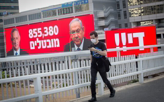 Un homme portant un masque de protection passe devant un panneau indiquant le nombre de chômeurs en Israël, à côté du mot "Assez !" à Tel Aviv, le 22 juillet 2020. (Miriam Alster/Flash90)