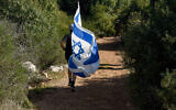 Un homme court avec le drapeau israélien dans la forêt de Reihan à côté de Tal Menashe, en Cisjordanie, où Esther Horgen a été retrouvée morte dans un attentat terroriste présumé, le 21 décembre 2020. (Crédit : Flash 90/Meir Vaknin)