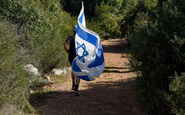 Un homme court avec le drapeau israélien dans la forêt de Reihan à côté de Tal Menashe, en Cisjordanie, où Esther Horgen a été retrouvée morte dans un attentat terroriste présumé, le 21 décembre 2020. (Crédit : Flash 90/Meir Vaknin) Un homme court avec le drapeau israélien dans la forêt de Reihan à côté de Tal Menashe, en Cisjordanie, où Esther Horgen a été retrouvée morte dans un attentat terroriste présumé, le 21 décembre 2020. (Crédit : Flash 90/Meir Vaknin)