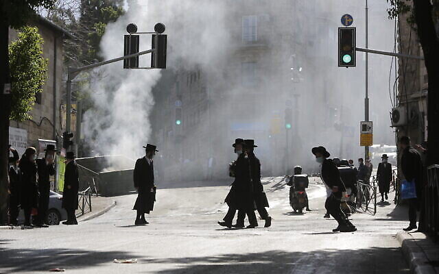 Des hommes marchent dans un nuage de fumée provenant de l'incendie d'une poubelle dans un quartier ultra-orthodoxe de Jérusalem, le 24 janvier 2021. (Crédit : AP Photo/Sebastian Scheiner)