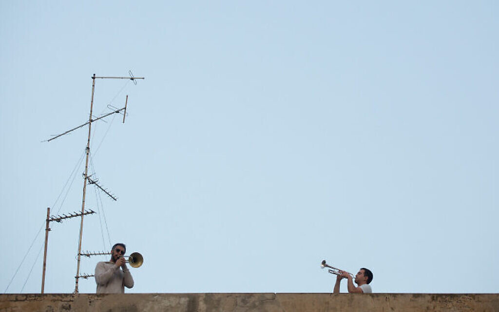 Les Israéliens écoutent depuis leur balcon le saxophoniste Yarden Klayman lors d'un concert donné sur un toit de la place Basel à Tel Aviv, le 23 mars 2020. (Crédit : Miriam Alster/Flash90)
