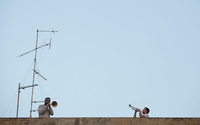 Les Israéliens écoutent depuis leur balcon le saxophoniste Yarden Klayman lors d'un concert donné sur un toit de la place Basel à Tel Aviv, le 23 mars 2020. (Crédit : Miriam Alster/Flash90)