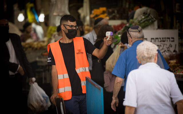 Illustration : Un homme vérifie la température d'un client à l'entrée du marché Mahane Yehuda à Jérusalem, le 18 juin 2020. (Yonatan Sindel/Flash90) Illustration : Un homme vérifie la température d'un client à l'entrée du marché Mahane Yehuda à Jérusalem, le 18 juin 2020. (Yonatan Sindel/Flash90)